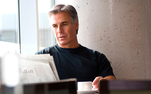 Gray haired middle aged man reading newspaper in cafe on weekend.